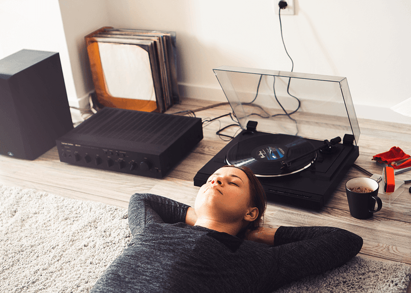 A young woman lying down listening to a record player.